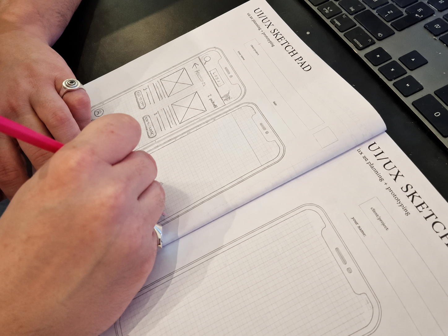 Hand drawing UI/UX wireframes on a sketch pad with a pink pencil
